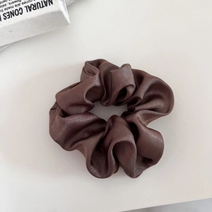Detail of glossy satin scrunchie fabric texture and premium brown silk luster