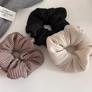 Three elegant ribbed scrunchies in black, cream, and taupe on a white surface