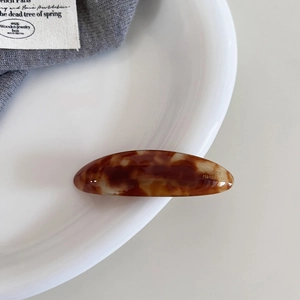 Detailed view of handmade amber tortoiseshell oval hair clip on white porcelain plate