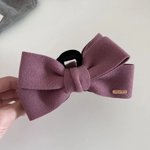 Macro detail of purple wool bow hair claw clip featuring golden Hand Made metal tag