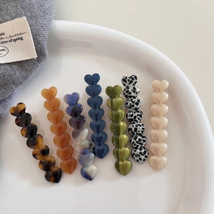 Set of seven colorful heart-shaped acetate hair clips in a stylish white ceramic tray