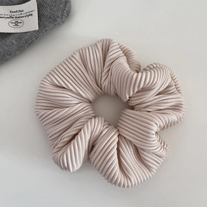 Detail of beige ribbed fabric scrunchie showing fine pleated texture and soft material