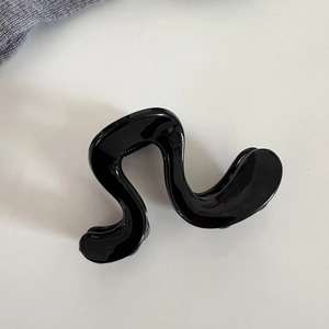 Détail d'une pince à cheveux noire brillante au design ondulé moderne sur fond blanc pur