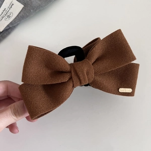 Brown wool-like bow hair claw clip with golden handmade label for elegant hairstyling
