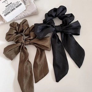 Dettaglio di elastici per capelli in raso nero e marrone con fiocchi luccicanti