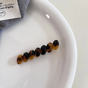Detail view of oval tortoiseshell acetate hair clip on a white ceramic dish