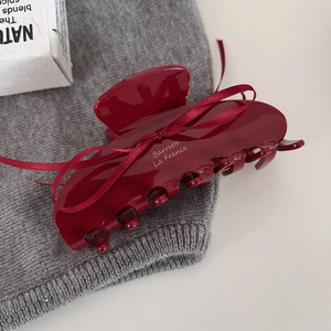 Detail of red hair claw with golden lettering and ribbon on grey knit fabric