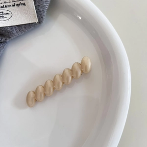 Macro detail of cream twisted bead hair clip on a white ceramic tray with elegant styling