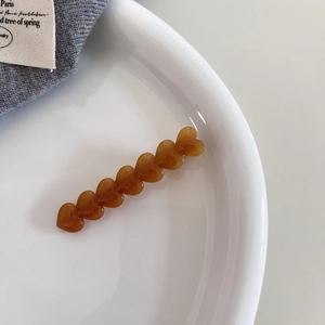 Detailed view of amber acetate hair clip with seven hearts on minimalist ceramic plate