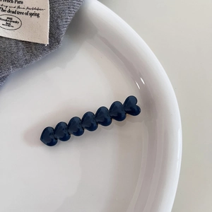 Detailed macro view of dark blue heart-shaped acetate hair clip on a white ceramic tray