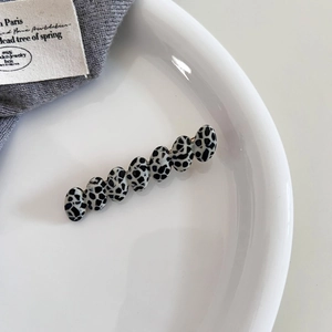 Detail view of oval acetate hair clip with black and white cow pattern on a white plate