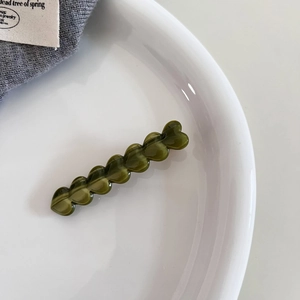 Macro view of olive green acetate hair clip with heart-shaped design on ceramic tray