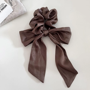 Dettaglio dello scrunchie in raso marrone scuro con fiocco grande e trama luccicante