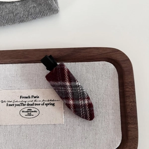 Vintage red and grey checkered wool hair clip on a minimalist wooden display tray