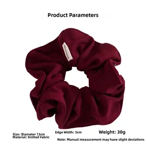 Detail of dark red knitted scrunchie with handmade label and 13cm diameter measurement