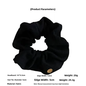 Detail view of black ribbed knit scrunchie featuring a round bronze metal logo emblem