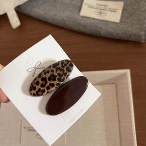 Dettaglio di fermagli per capelli ovali con stampa leopardata e marrone scuro su carta