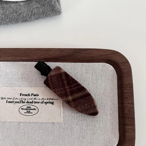 Detail of coffee-colored plaid wool fabric hair clip on a wooden jewelry display tray