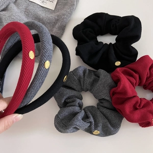 Close-up of ribbed knit scrunchies and headbands with gold logo buttons in red, black, and gray