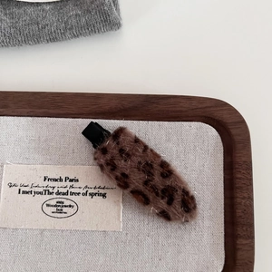 Detailed close-up of a leopard print plush hair clip on a walnut display tray