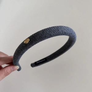 Detailed close-up of a grey ribbed knit headband with gold logo and handmade tag