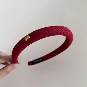 Detail of burgundy knitted headband featuring gold metal logo and handmade inner tag
