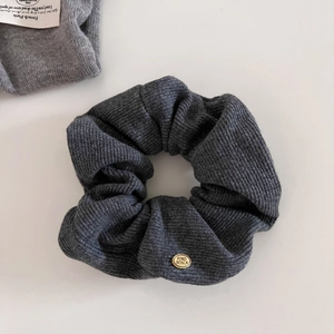 Dark grey knitted scrunchie with a gold logo charm on a clean white background