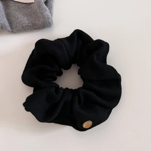 Detail of black ribbed knit scrunchie featuring a circular gold metal logo branding