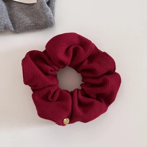 Detail of burgundy ribbed fabric scrunchie with a round gold metal tag embellishment
