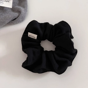Close-up of black ribbed knit scrunchie featuring a handmade label and soft texture