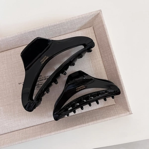 Detail of glossy black acetate hair claws with gold handmade lettering on a beige tray