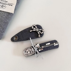 Dettaglio di fermagli in maglia grigia con fiocco di cristallo e placca logo in metallo