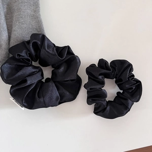 Détail de deux chouchous en satin noir avec une texture soyeuse élégante et étiquette tissée