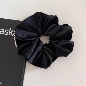 Dettaglio macro di un grande elastico scrunchie in seta nera con pieghe morbide