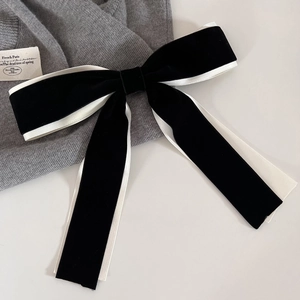 Close-up of elegant French black velvet hair bow with white satin edges and spring clip