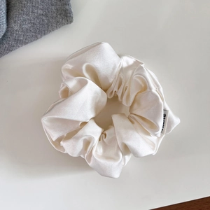 Détail du chouchou en satin ivoire montrant la texture brillante et l'étiquette tissée