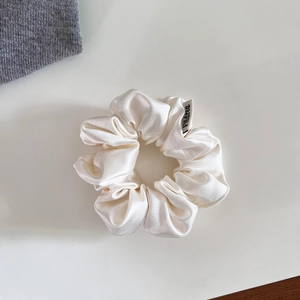 Vue détaillée d'un chouchou en satin blanc soyeux avec des plis élégants et étiquette de marque
