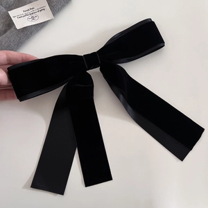 Detail of a large black velvet bow hair clip with elegant satin edges and long streamers