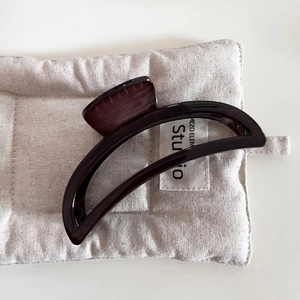 Detailed view of a dark coffee wood-grain hair claw clip on a soft quilted beige fabric background