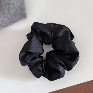 Gros plan d'un chouchou en satin noir avec texture brillante et étiquette de marque