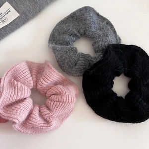 Close-up of knit scrunchies in pink, grey, and black showing soft wool texture