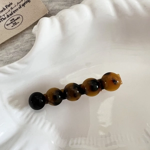 Détail d'une pince à cheveux en acétate écaille avec cinq perles sur plateau céramique