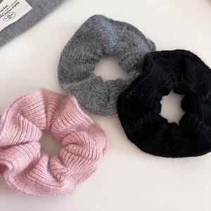 Close-up of three soft knit hair scrunchies in pink, grey and black with fuzzy texture
