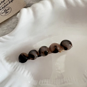 Détail macro des perles rondes en acétate écaille sur une pince à cheveux dorée