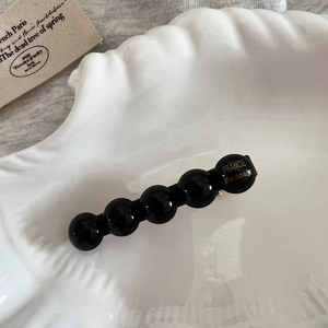 Détail d'une pince à cheveux avec perles en résine noire et lettrage doré fait main