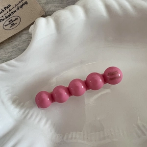 Détail d'une pince à cheveux à perles roses en acétate sur un plateau en coquillage blanc