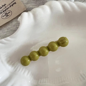 Vue détaillée de perles de résine vert olive sur pince à cheveux dorée dans un plateau