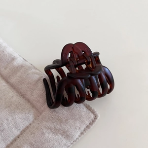 Detail view of glossy tortoiseshell pumpkin hair claw clip on a soft quilted surface