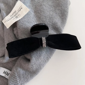Dettaglio del fermaglio per capelli a fiocco in velluto nero con strass su tessuto grigio