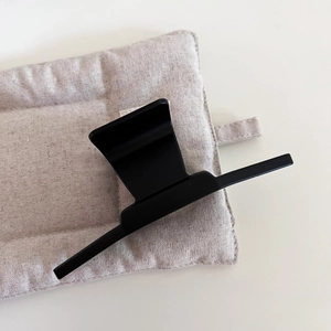 Detail of a large matte black shark clip on a textured fabric background for hair styling